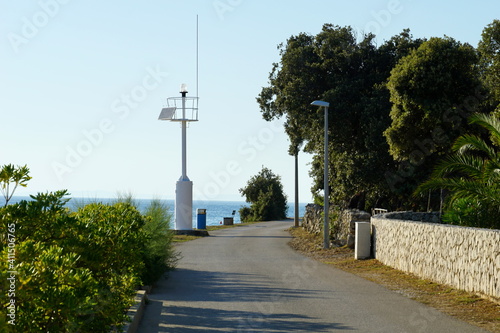 Promenade by the sea with a small white lighthouse in a coastal village © Happy window