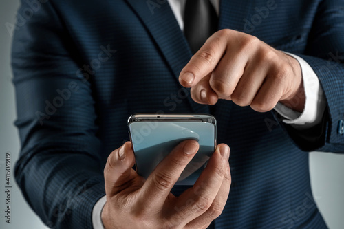 A businessman in a business suit holds a smartphone in his hands. Uses the Internet to work and communicate with partners. Online business concept, remote work, freelance. Close-up. © Aliaksandr Marko