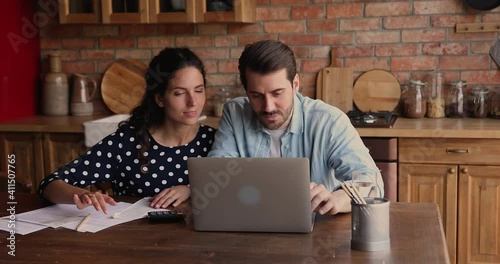 Married couple sit in kitchen at home check receipts, paying monthly domestic utility bills using e-bank application on laptop, provide monthly remittance. Family budget plan and management concept photo