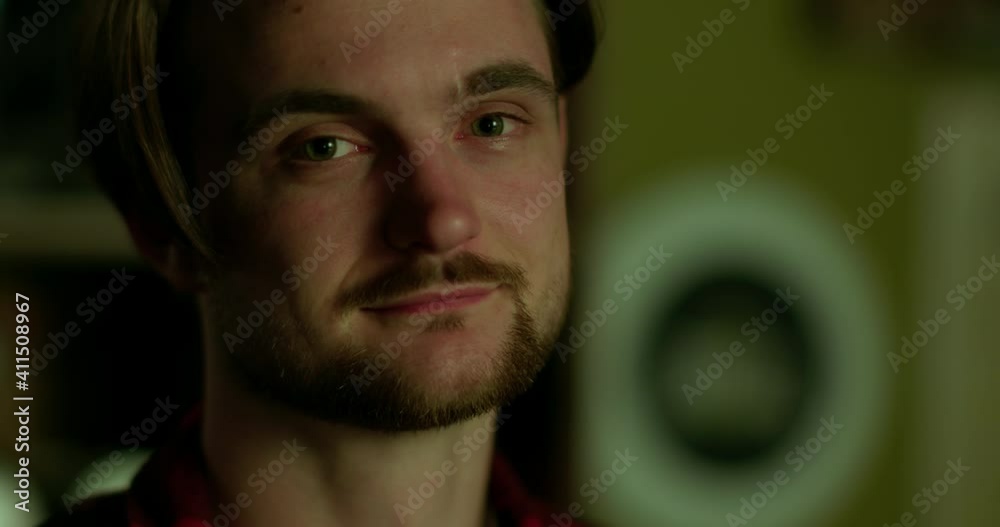 Close up portrait of young male face, looking calm, confident, kind at the camera indoor in the evening.