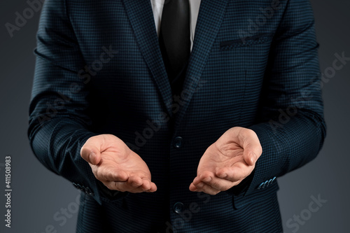 Male hand in a suit shows a palm up gesture on a gray background. Concept of request, bankruptcy, close-up.