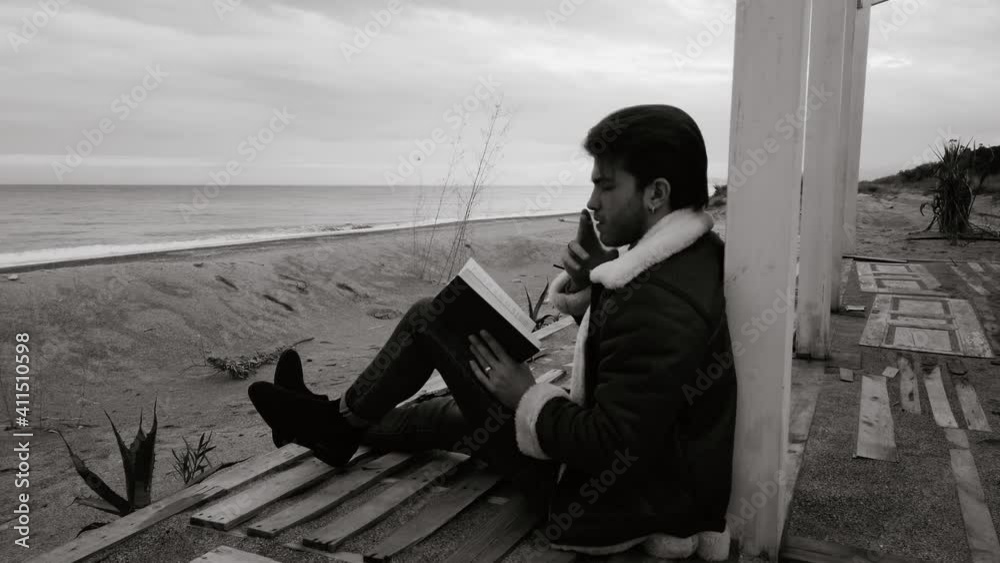 Ragazzo legge un libro e fuma una sigaretta seduto in riva al mare in spiaggia