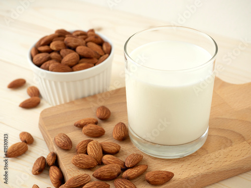 Organic almonds milk in glass and heap almond nuts on wood cutting board and almonds in white ceramic bold on wooden table for almond nuts can improve health concept.