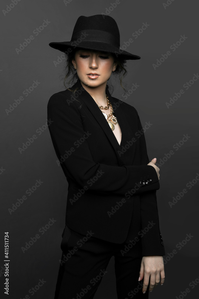 Front portrait of young splendid brunette woman in black suit and hat with makeup, curly hair, over grey background. Front portrait of young splendid brunette woman in black suit and hat with makeup, curly hair, over grey background.