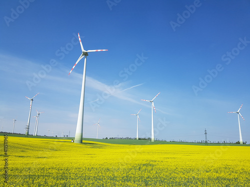 Wind power plants in a field of yellow flowers under a blue sky. photo