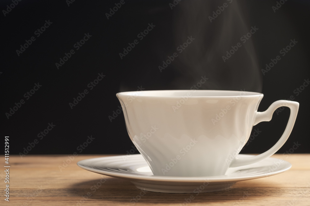 A white cup of coffee or tea with smoke on old wooden table on black background. Hot drink. A white cup of coffee or tea with smoke on old wooden table on black background. Hot drink.