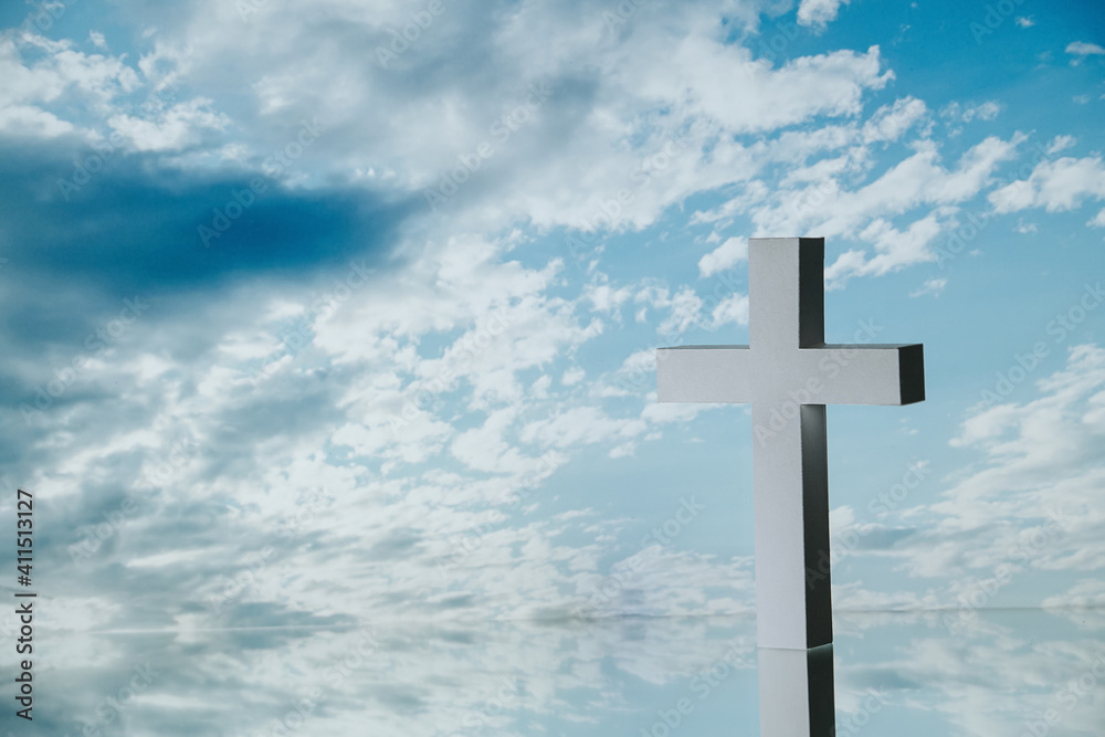 White cross against blue clouded sky. It's standing on a reflective surface. White cross against blue clouded sky. It's standing on a reflective surface.