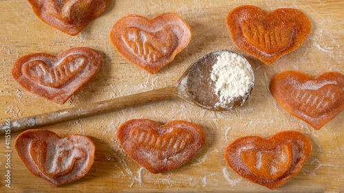 Special pasta for Valentine's day. Made with love, fresh heart formed tortellini with tomato filling on a wooden kitchen cutting board.  Creative food concept. Close up.