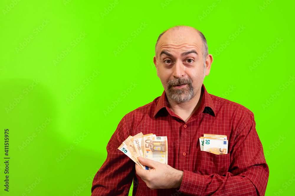 Middle-aged Caucasian man holding a bunch of 50 euro bills in his hand and has more in his shirt pocket. He is happily surprised. Concept of winning, luck and wealth. Yellow background. Middle-aged Caucasian man holding a bunch of 50 euro bills in his hand and has more in his shirt pocket. He is happily surprised. Concept of winning, luck and wealth. Yellow background.