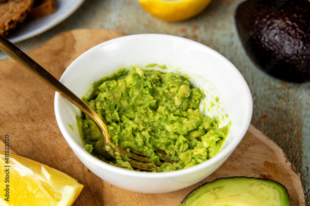 Close up of mashed avocado in a plate with fork on cooking table. Healthy vegan food concept. High saturated fats can help to maintain healthy cholesterol levels. Brain food Close up of mashed avocado in a plate with fork on cooking table. Healthy vegan food concept. High saturated fats can help to maintain healthy cholesterol levels. Brain food