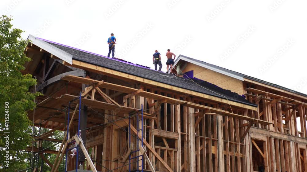 Timelapse from below of group of builders applying soft tiles on the frame house roof Timelapse from below of group of builders applying soft tiles on the frame house roof