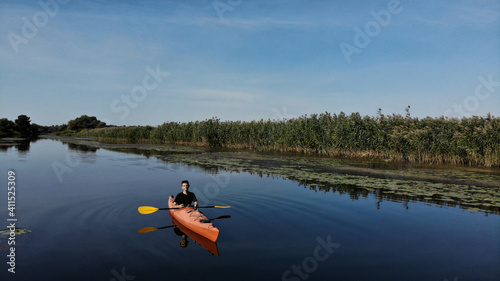 Aerial view of young man floats on an orange kayak on the river. The banks of the river are overgrown with reeds. Ukraine, Europe © Yevheniia Kudrova