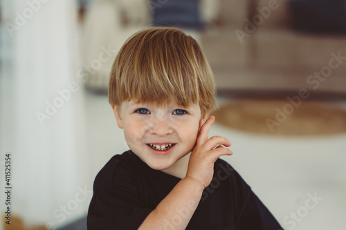 close portrait of cute smiling 3 year old blond boy with blue eyes wearing black t-shirt indoor
