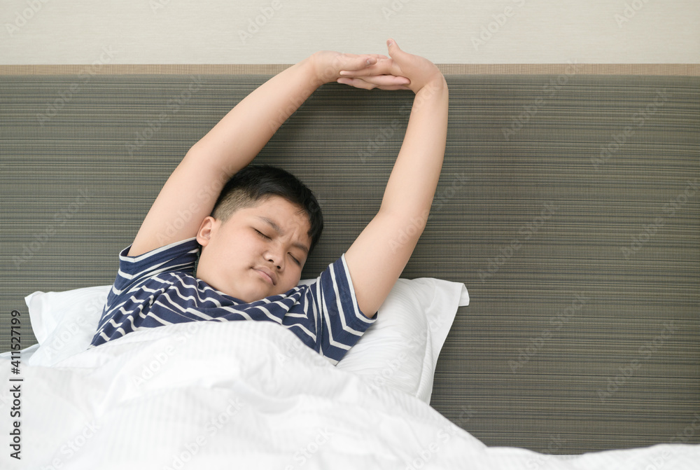 obese fat boy wakes up and stretching on bed in morning,
