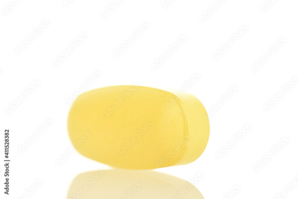 One oval yellow tablet, close-up, isolated on white.