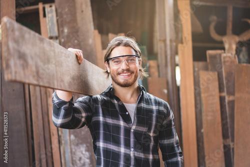 Fotobehang young male carpenter worker smiling while hold wooden plank at the carpentry wor
