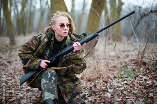 caucasian woman in camouflage suit and sunglasses with shotgun in the autumn forest