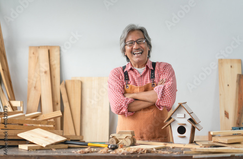Asian senior carpenter man with crossed arms smile at home carpentry workshop photo