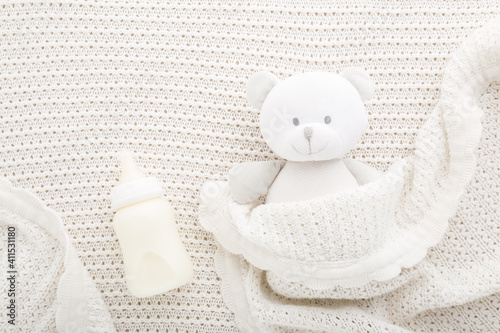 Teddy bear and bottle of milk on light white blanket. Baby feeding concept. Closeup. Top down view.