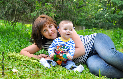 Young woman with her one-year-old baby, both dressed in striped T-shirts, sitting on a green lawn in a sunny park. Family time, motherhood, and bonding outdoors. Concept of parenting, childhood. photo