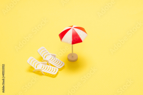 Two sun loungers and a red umbrella on a yellow background.