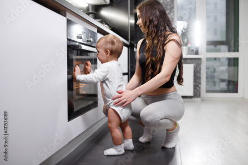 Young mother and her son open door of oven in kitchen with modern appliances and devices