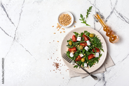 Healthy vegetarian salad with fresh arugula, cherry tomatoes, soft cheese, olives and pine nuts