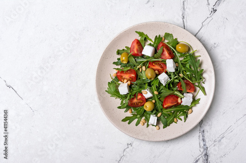 Healthy vegetarian salad with fresh arugula, cherry tomatoes, soft cheese, olives and pine nuts