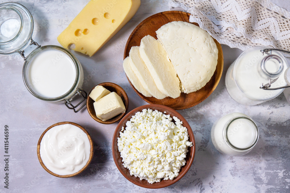 Set of different dairy products (milk, sour cream, cottage cheese, yogurt and butter) on a light stone countertop. Top view flat lay.