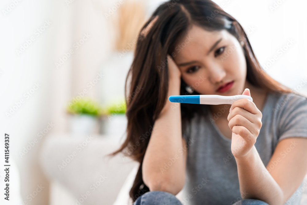 Asian woman sitting bed feeling disappointed when see the pregnancy test result. Woman feels worry and not ready to be a mother. Man feeling stress about the future kid holding head Asian woman sitting bed feeling disappointed when see the pregnancy test result. Woman feels worry and not ready to be a mother. Man feeling stress about the future kid holding head