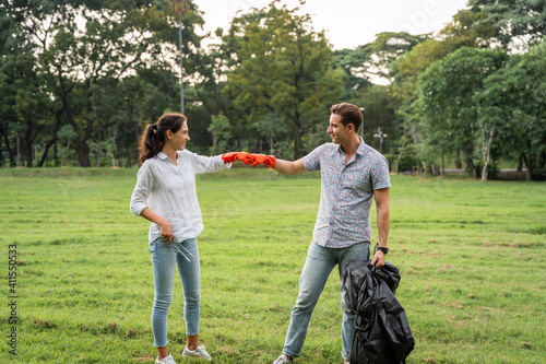 Volunteer lovers couple wearing gloves walking to to pick up garbage in the park To keep the environment clean