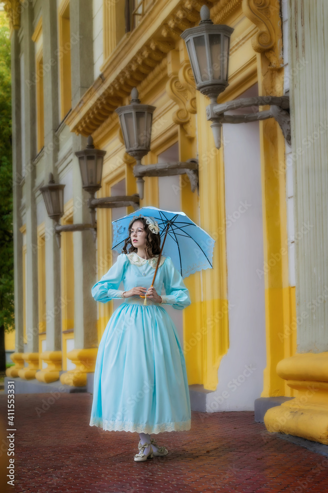 Girl in a vintage dress with an umbrella near mansion