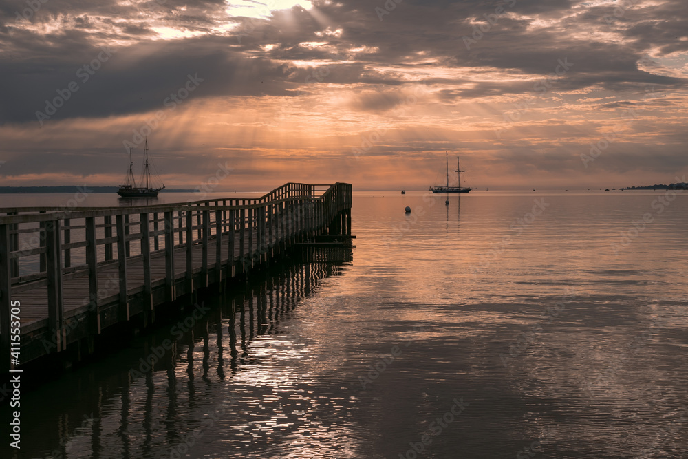 Obraz premium Silhouette of pier and sailing ships with epic sunburst.