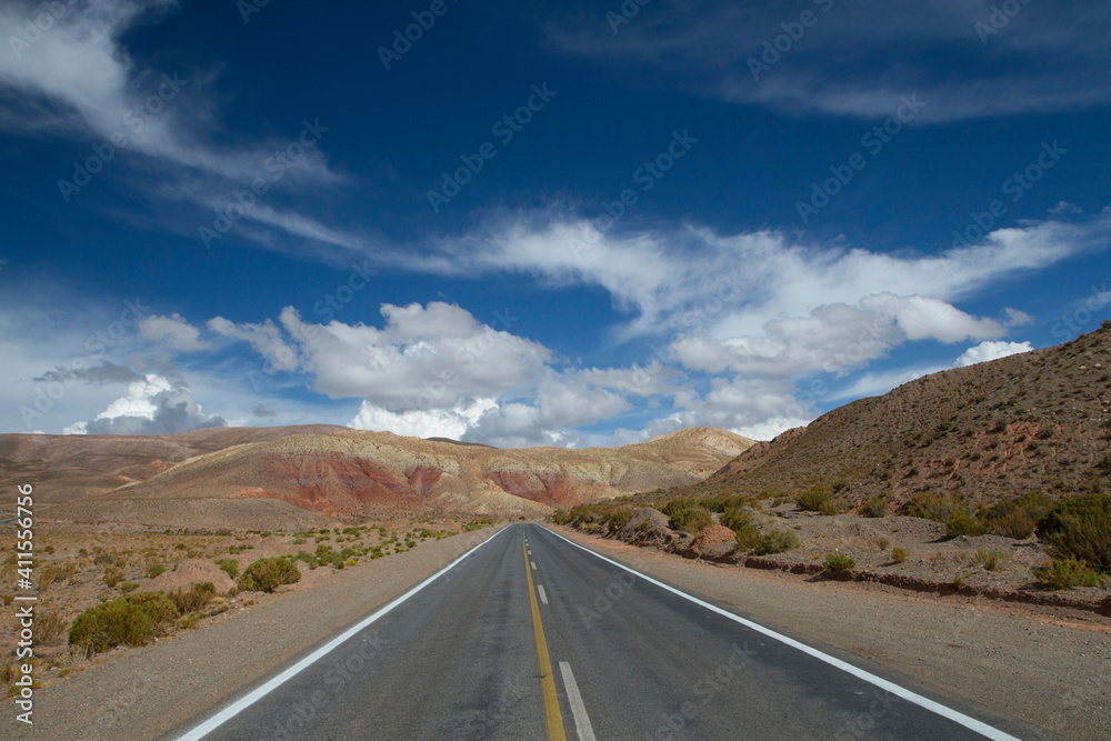 Road trip into the wild. Driving along the desert asphalt route across the arid desert and colorful mountains under a beautiful blue sky.  