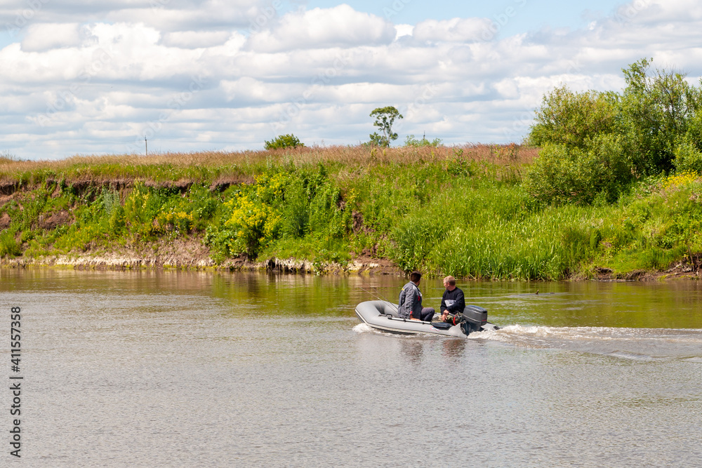 Fishermen sail in an inflatable boat with an outboard motor on a summer river. Fishermen sail in an inflatable boat with an outboard motor on a summer river.
