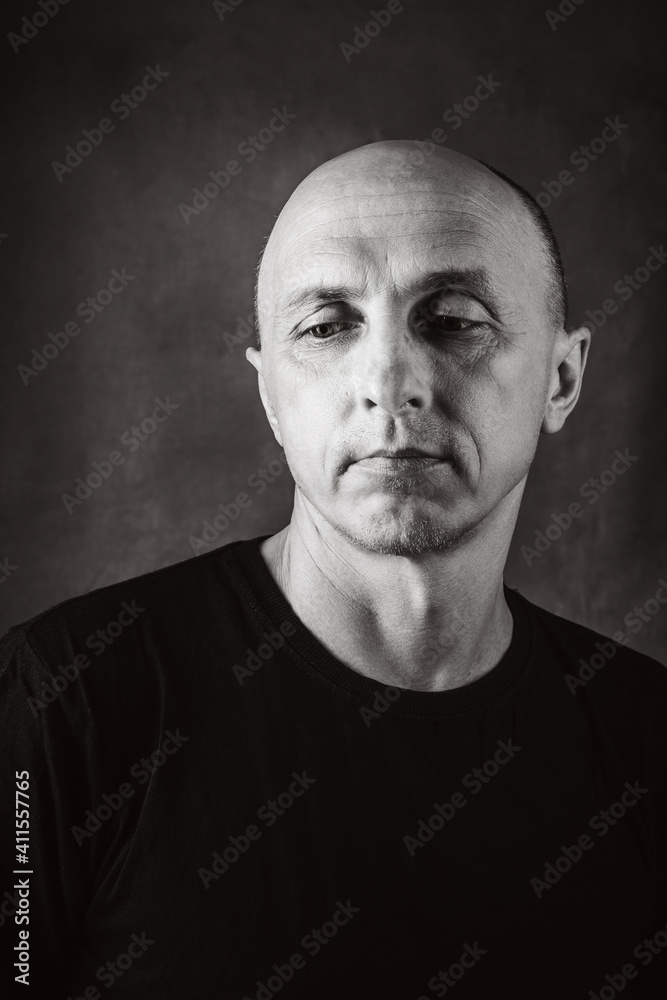 A serious middle-aged man with an unshaven face and a bald head looks thoughtfully to the side. Black and white portrait toned in sepia. Photo taken in studio