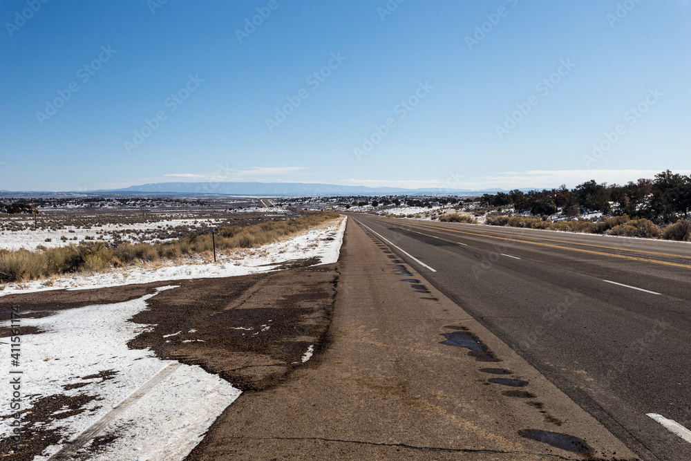 Empty highway cutting through snow covered wide open desert vista on clear day in rural New Mexico
