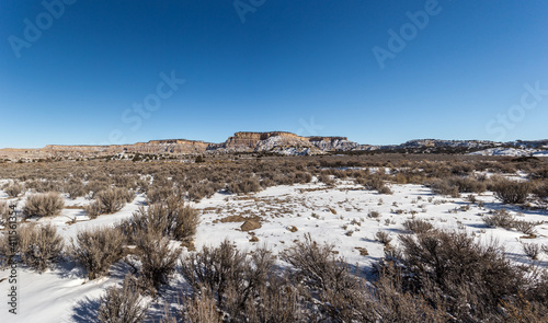 Panoramic view of wide open desert vista covered in snow with mountain range on clear day in rural New Mexico