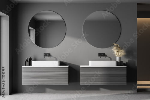 Interior of modern bathroom with dark gray walls, concrete dark floor, sink with round mirror and cabinets. Concept of spa.