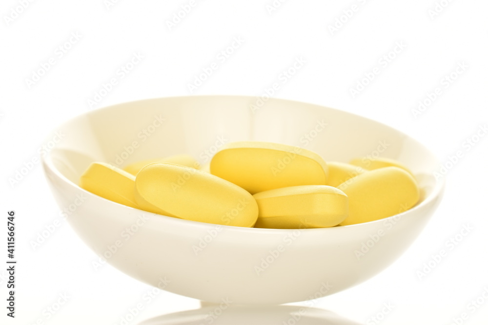 Several oval yellow tablets in a ceramic
 saucer, close up, isolated on white.