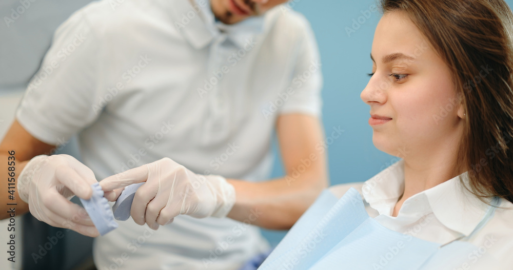 Fototapeta premium Dentist showing a jaw model, explaining to the young patient the process of orthodontic treatment. Girl with dental braces with a dentist. 4k video screenshot, please use in small size