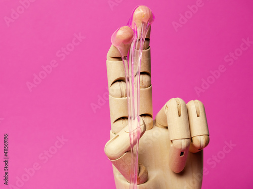 Close-up wooden hand with dripping pink liquid paste pink background. Hair removal and sex concept.