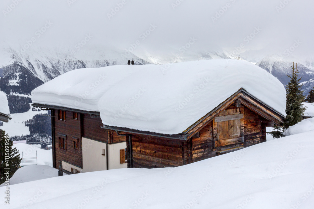 Alpine chalet sunk in deep snow in winter with thick snow on roof in the Swiss Apls, Switzerland