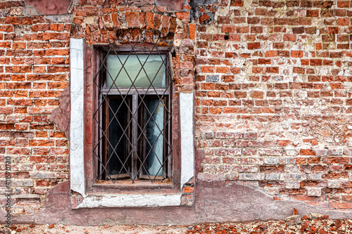 Window with a rusty grate on the crumbling brick wall of an abandoned house