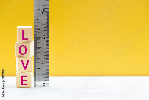 Measurement of love, quality and quantity, behavioral science concept : Square wood blocks with a word LOVE are measured by a metal ruler with centimeter scale over yellow background