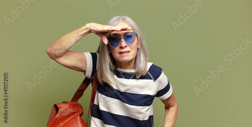 senior woman looking bewildered and astonished, with hand over forehead looking far away, watching or searching