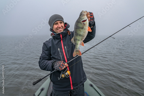 Happy fisherman hold big perch fish at boat with tackle. Success fishing at wild lake