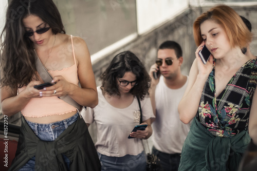 Group of friends talk on smartphones while standing on escalator. Modern people with cell phones outdoor. Mobile communication technology. High angle view