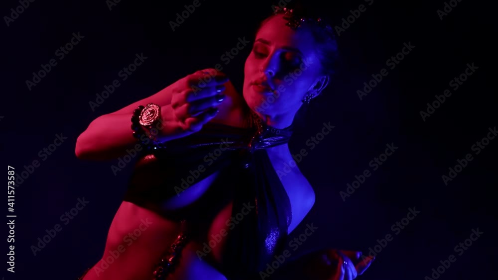 An attractive woman is dancing an oriental dance on a black smoky background in the studio, making beautiful movements with her hands. An attractive woman is dancing an oriental dance on a black smoky background in the studio, making beautiful movements with her hands.