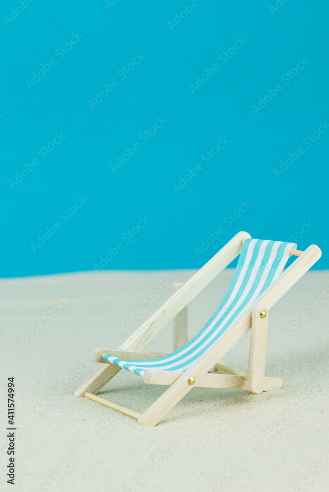 Beach relaxation and vacation concept. Toy sun lounger on sand and colorful paper background. Beach relaxation and vacation concept. Toy sun lounger on sand and colorful paper background.